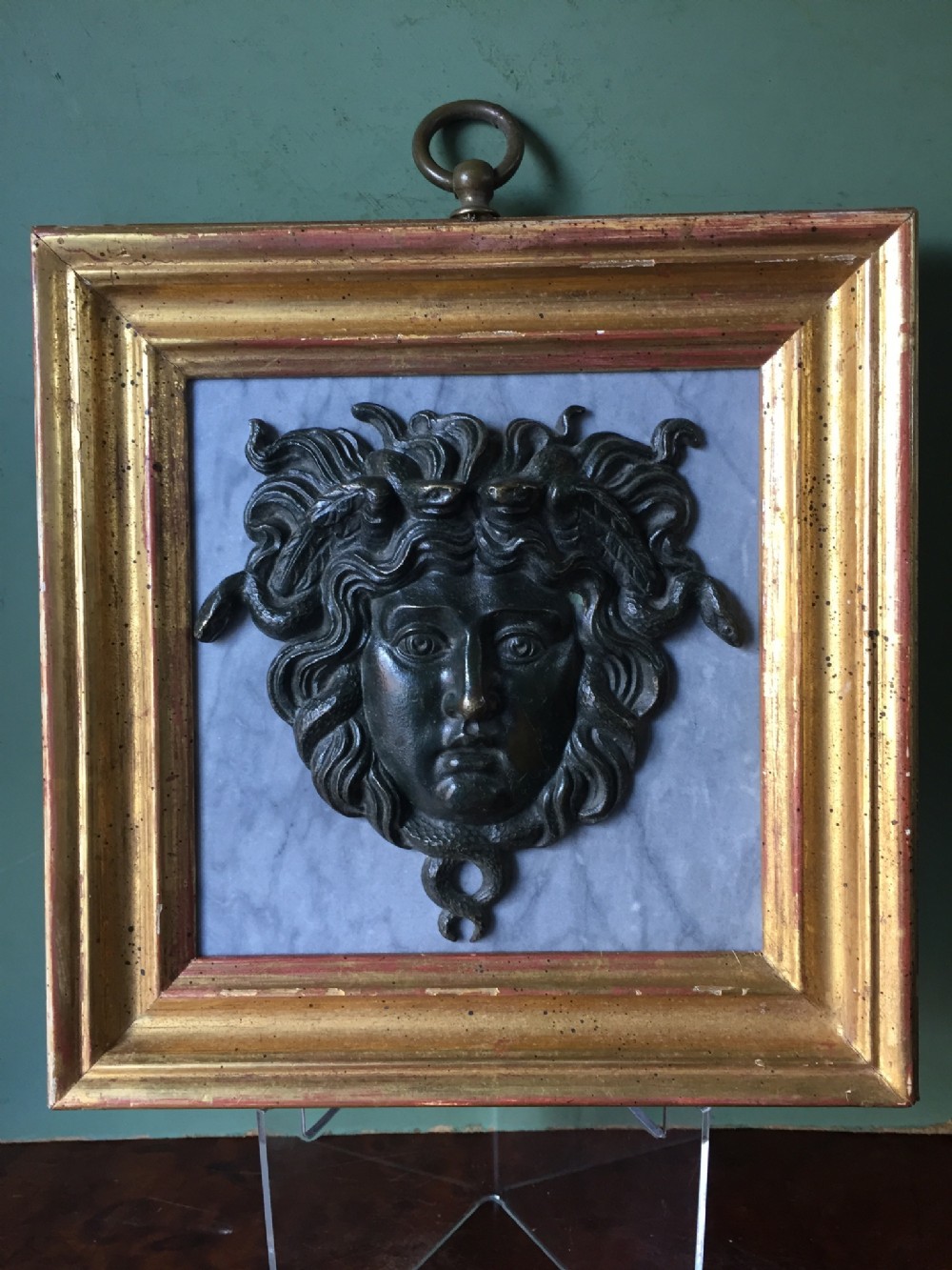 c19th 'grand tour' souvenir bronze mask of medusa mounted upon a pale grey marble panel and set in a giltwood frame