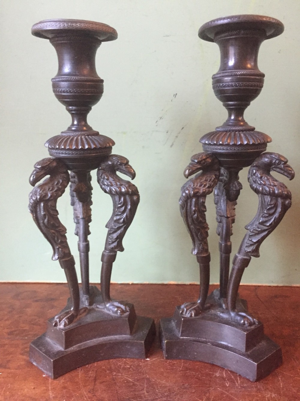 pair of early c19th george iv period bronze candlesticks on triform stylised eagle or griffin supports