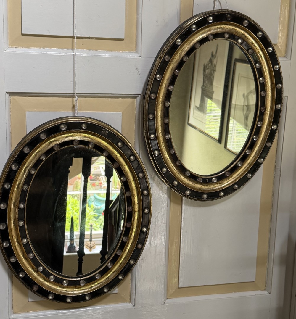 scarce pair of early c19th irish oval ebonised parcelgilt and glass cabochon mounted mirrors of smaller scale